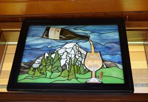 Stained glass of a bottle of Blakeslee wine being poured into a glass in front of a mountain with trees